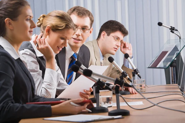 Quatro jovens bem-sucedidos sentados em uma fila na frente de monitores falando em microfones — Fotografia de Stock