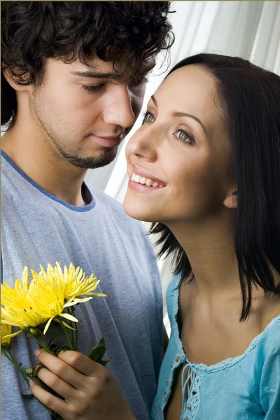 노란색 꽃을 들고 그의 웃는 여자 친구를 껴 안은 젊은 사랑 하는 갈색 머리 남자 — 스톡 사진