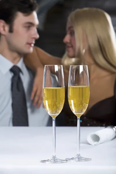 Dois copos de champanhe na mesa e casal amoroso no fundo — Fotografia de Stock