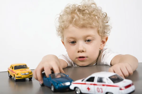 Curly menino loiro brincando com carros na mesa cinza — Fotografia de Stock
