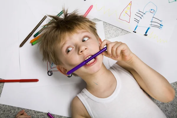 Laughing boy lying on his drawing with felt-tip pen in his teeth — Stock Photo, Image