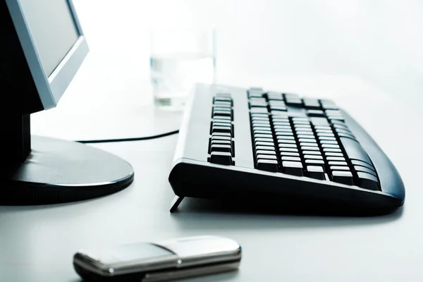 Imagem do teclado, monitor, célula e um copo de água na mesa — Fotografia de Stock