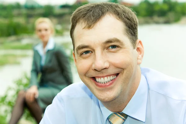 Portrait of cheerful young man sitting on grass and smiling — Stock Photo, Image