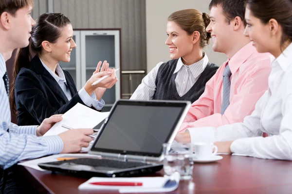 Image of laptop on workplace with associates talking on background Stock Photo