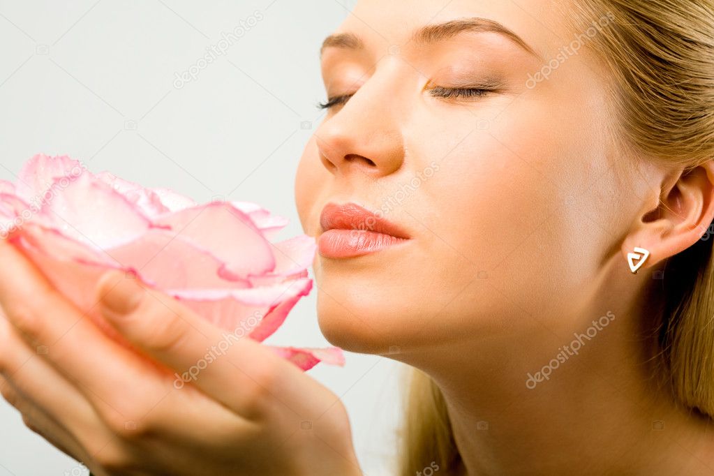 Young pretty woman enjoys a smell of a pink rose
