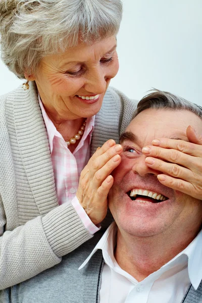 Pretty senior wife closes husband's eyes by hands — Stock Photo, Image