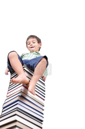 Mignon petit garçon assis sur une grande pile de livres 