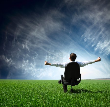 Jeune homme assis sur une chaise dans la prairie verte 