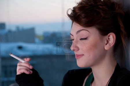 Belle jeune femme fumant sur la fenêtre du soir .