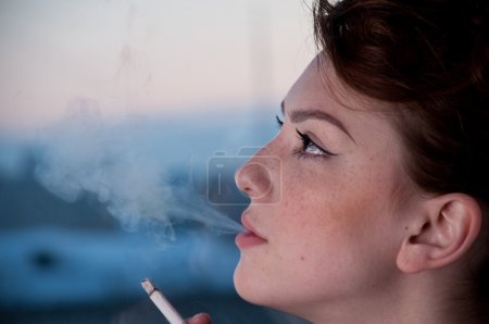 Belle jeune femme fumant sur la fenêtre du soir .