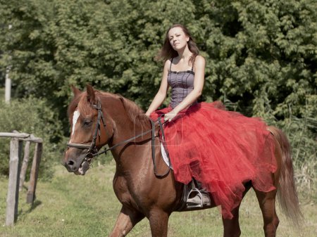 Une fille en jupe rouge assise sur un cheval 