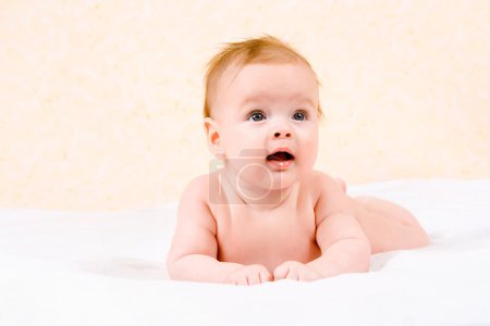 Bébé heureux couché sur son ventre, sourit et lève les yeux 