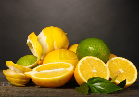 citrons mûrs et citrons verts avec des feuilles sur table en bois sur fond gris 