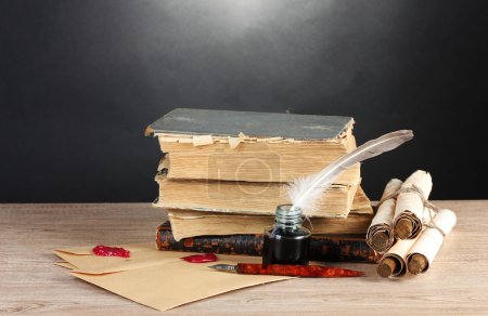 Livres anciens, rouleaux, plume et encrier sur table en bois sur fond gris 