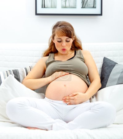 Belle femme enceinte assise sur le canapé et soufflant baiser son ventre .