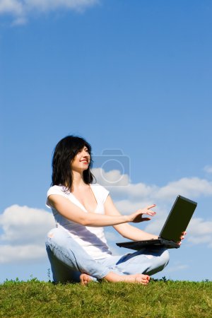 jolie femme avec ordinateur portable sur l'herbe verte 